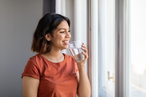 Smiling,Young,Arab,Female,Drinking,Water,From,Glass,While,Standing